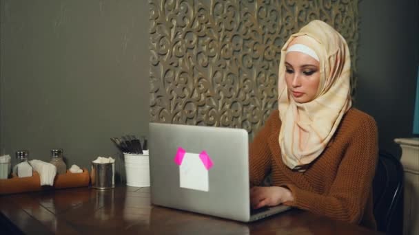 Moderne arabische Frau im hellen Hidschab arbeitet mittags im Café am Laptop — Stockvideo
