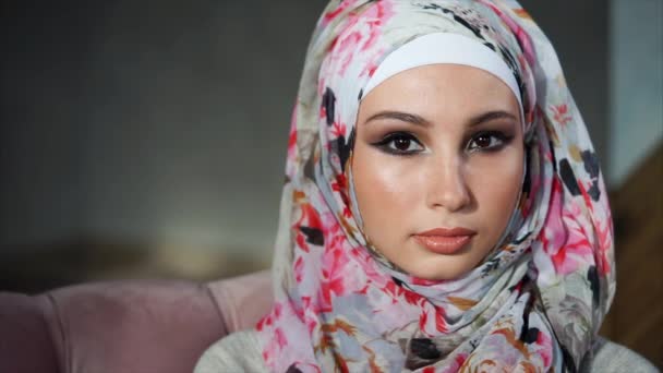 Young Muslim woman with painted eyes in hijab, looks at camera and blinks slowly — Stock Video