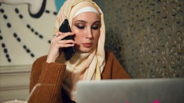 Modern Müslüman cep telefonundan kafede dizüstü bilgisayar ile çalışırken kadındır