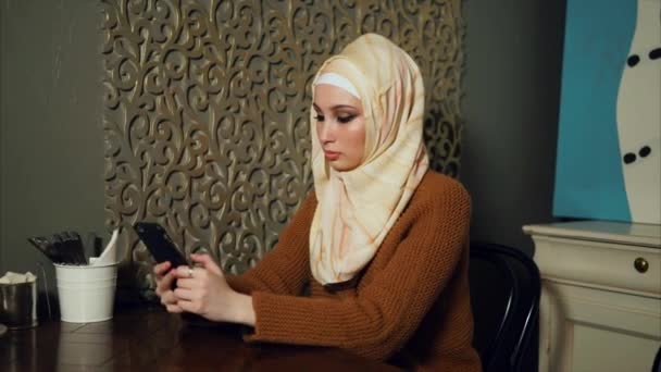 Unga muslimska kvinnan med smart telefon i café — Stockvideo