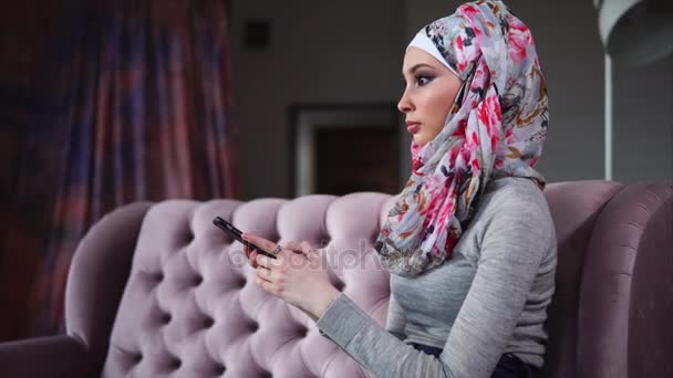 家庭での携帯電話でインターネットをサーフィン ヒジャーブでイスラム教徒の女性 — ストック動画