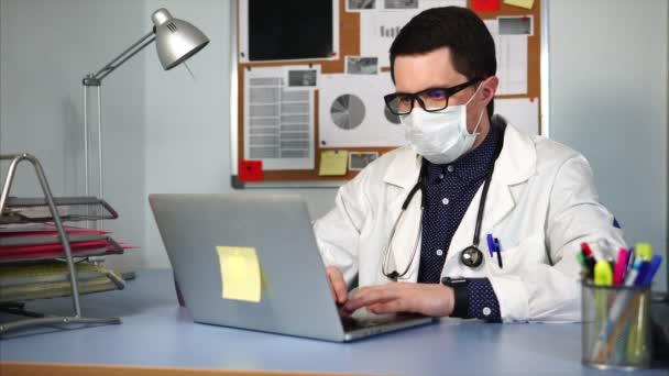 Médico con máscara médica sentado en el lugar de trabajo . — Vídeo de stock