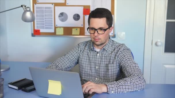 Νεαρός άνδρας κάθεται στο γραφείο σε γραφείο, λειτουργεί σε φορητό υπολογιστή. — Αρχείο Βίντεο