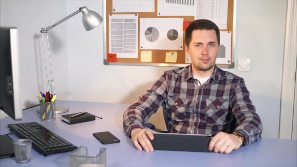 De manager van het bedrijf zit aan de tafel waar de tablet, mobiele telefoon — Stockvideo