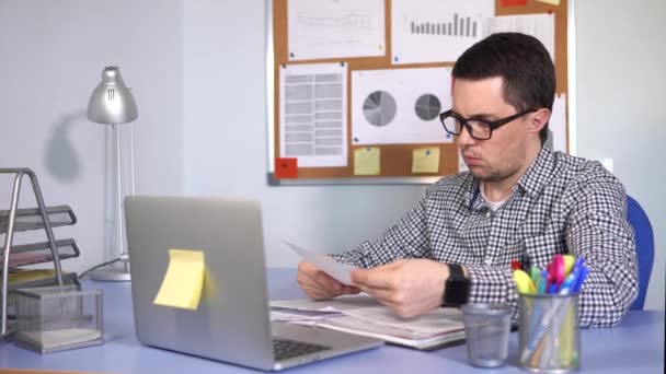 Босс проверяет документы, сидящие за столом, где стоит ноутбук. — стоковое видео