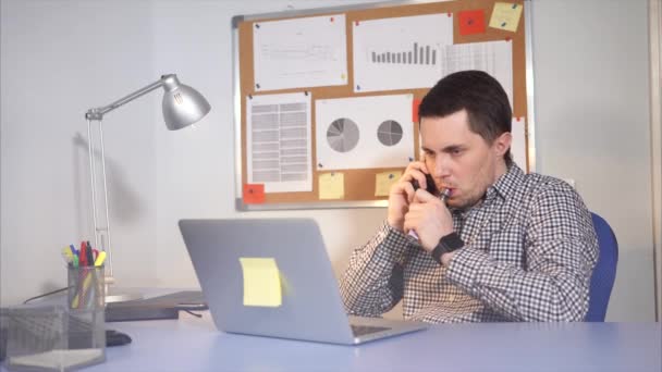 Un hombre fuma un cigarrillo electrónico en una habitación de la oficina, mirando un ordenador portátil — Vídeo de stock