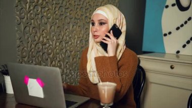 Dizüstü bilgisayarda çalışan ve Smartphone'da konuşuyor Modern Arap iş kadını.