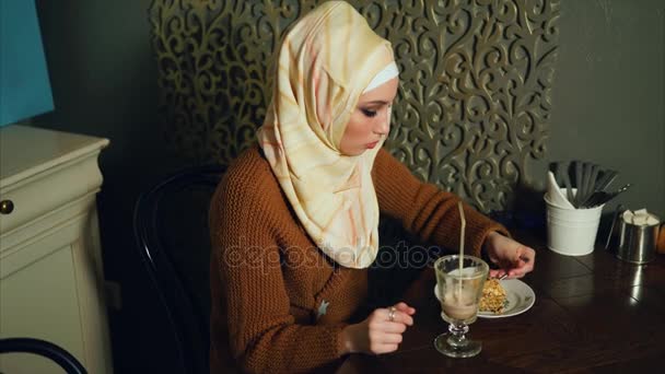 Una mujer musulmana moderna come postre y bebe un cóctel de chocolate en un café — Vídeo de stock