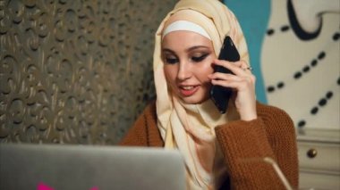 Modern Müslüman cep telefonundan kafede dizüstü bilgisayar ile çalışırken kadındır