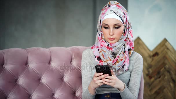 Schöne muslimische Frau mit leuchtend buntem Hijab, sitzt auf rosa Sofa — Stockvideo