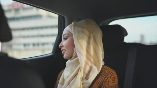 Mujer musulmana feliz en un coche en un asiento trasero de pasajero . — Vídeo de stock