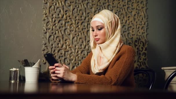 Moderne muslimische Frau im Hidschab im Café. Araberin nutzt Smartphone. — Stockvideo