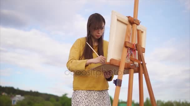 Jonge en creatieve kunstenaar schildert een foto op canvas in een open lucht — Stockvideo