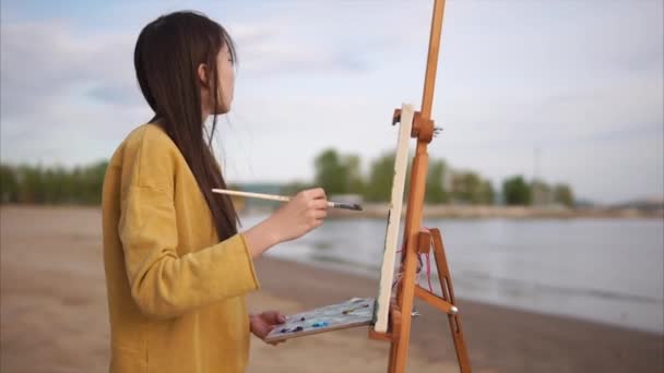 Μια νεαρή γυναίκα ζωγραφίζει ένα πινέλο με ένα ακόμα-ζωή σε ένα καβαλέτο, στον ανοιχτό αέρα — Αρχείο Βίντεο