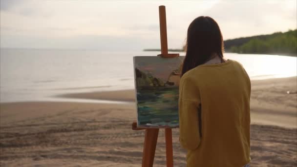 Молодий художник малює ножем палітри натюрморт дівчина знаходиться біля моря або річок — стокове відео