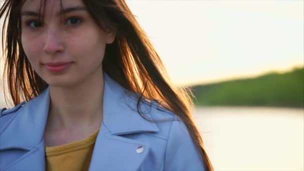 Retrato de una chica guapa que agita su pelo en el viento, está cerca de un lago — Vídeos de Stock