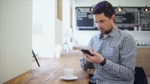 Een volwassen man communiceert op de telefoon zit in een koffiehuis — Stockvideo