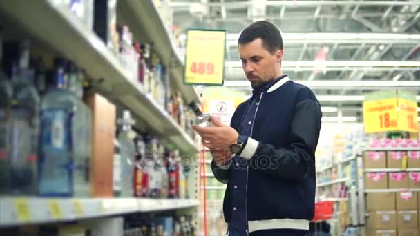 O homem adulto escolhe uma bebida alcoólica forte, a garrafa parece vodka — Vídeo de Stock