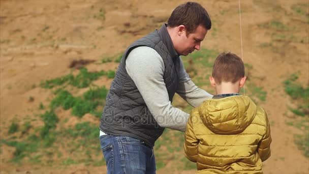 Семейная сцена. Человек помогает своему сыну контролировать воздушного змея и учить его — стоковое видео