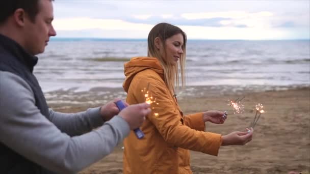 Família jovem com o filho queimar as luzes de Bengala perto do mar ao ar livre — Vídeo de Stock
