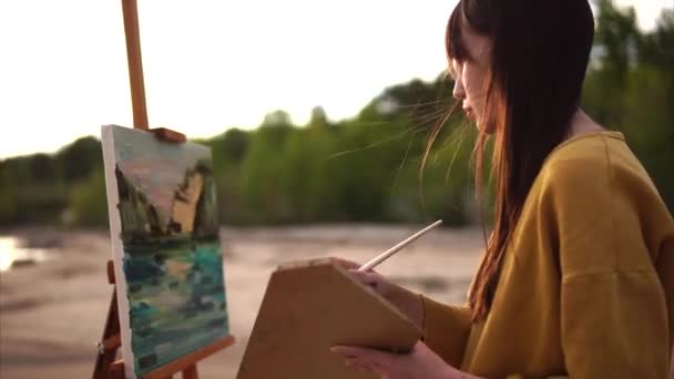 Joven artista dibuja una paleta cuchillo naturaleza muerta la chica está cerca del mar o ríos — Vídeo de stock