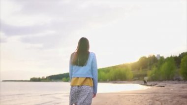 Kum ile ıssız bir kıyı boyunca ince bir genç modern giysiler içinde elini kolunu sallaya dönüyor