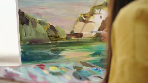 Uma jovem pinta uma pintura em tela, que fica em um cavalete — Vídeo de Stock