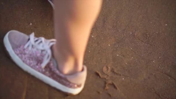 Nära upp skott av en flickor ben i sneakers som vandrar längs stranden. — Stockvideo