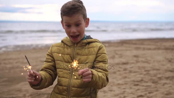 Un enfant heureux joue avec les lumières du Bengale sur la plage, il veut les éteindre — Video