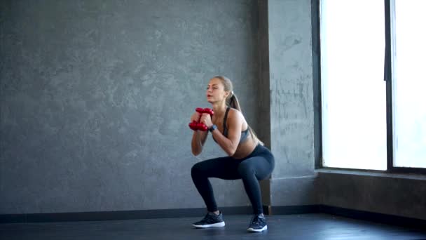 Joven mujer de fitness haciendo sentadilla con pesas en las manos. Escena en el gimnasio — Vídeos de Stock