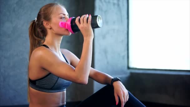 Beautiful girl in sport clothes drinking water after workout in the gym. — Stock Video