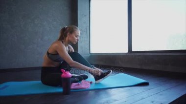 Genç atlet bağlama ayakkabı bağcığı spor ayakkabılar üzerinde bir halı için yoga bir Bayan oturuyor
