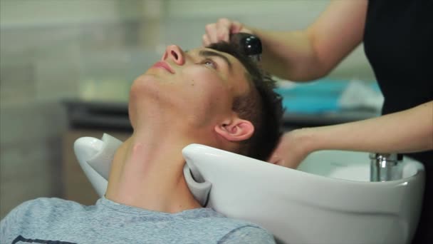 ヘアー スタイリストがシャンプー美容室に来た男性と、頭を洗う — ストック動画