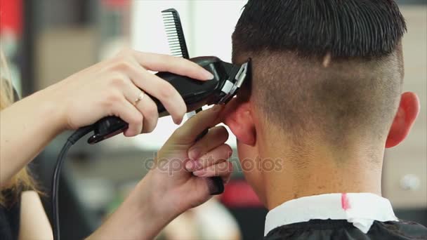 Um estilista que mantém um cortador de cabelo remove o excesso de cabelo da cabeça de um homem — Vídeo de Stock