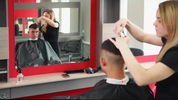 De stylist moderniseert het kapsel van een man, de vrouw prunks haar — Stockvideo