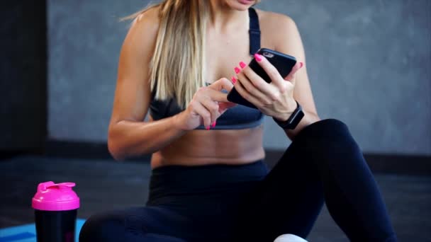 Vrouw in de sportschool na de oefeningen. Ze typen op de smartphone. — Stockvideo