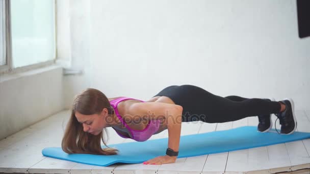 A young and pretty fitness trainer does push-ups from the floor in a sports club — Stock Video