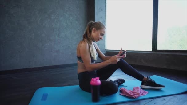 Bedrijf van de jonge dame die in de sportzaal gaat kijkt naar inkomende berichten op de telefoon — Stockvideo