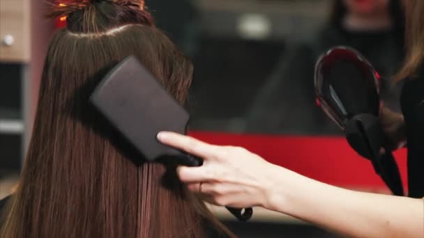 Ditembak dari tangan penata rambut, yang mengeringkan rambut dengan pengering rambut dan sisir — Stok Video