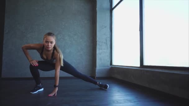 Mujer joven y atractiva haciendo estiramiento de los músculos de las piernas en el gimnasio — Vídeos de Stock