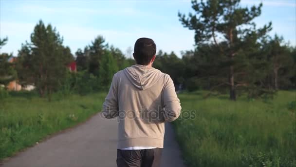Un hombre adulto con un traje deportivo corre a lo largo de un sendero en el parque en un día de verano — Vídeos de Stock