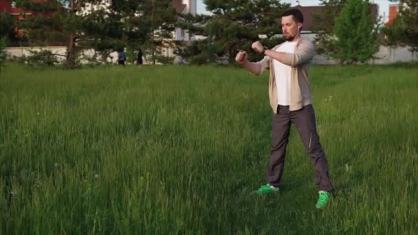 Un homme adulte fait un échauffement avant de commencer une séance d'entraînement, il se tient dans le parc — Video