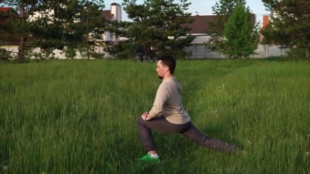 Взрослый мужчина в спортивной одежде делает упражнения в парке, слушает музыку — стоковое видео