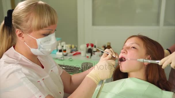 Een vrouw tandarts ervoor zorgt dat de tanden van een tiener die naar de orthodontist komen — Stockvideo