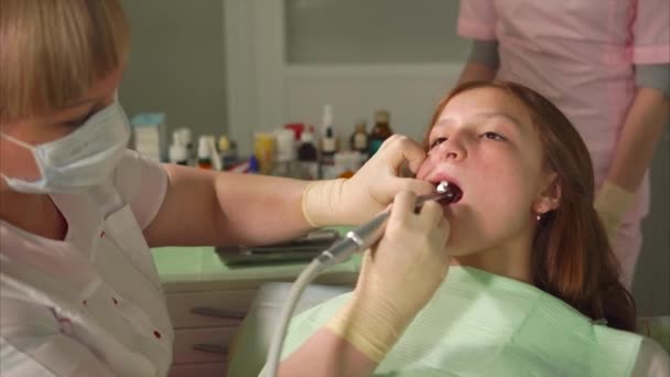 Een tandarts in latex handschoenen maalt tanden in een tiener met een metalen gereedschap — Stockvideo