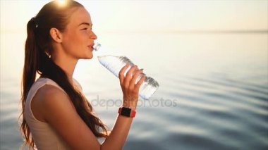 Genç mutlu gülümseyen kadın şişe denize yakın bir su içme.