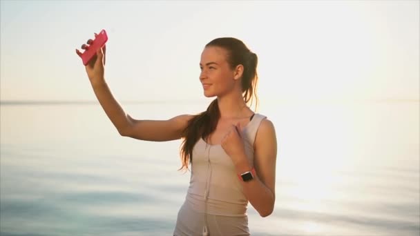 若い可愛い女性が海のそばのスマート フォンで selfie 写真を作る. — ストック動画