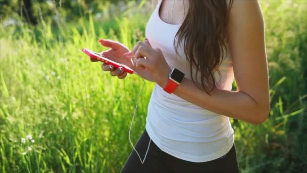 Jonge vrouw schrijft een bericht met behulp van haar smartphone. Groen gras achtergrond. — Stockvideo