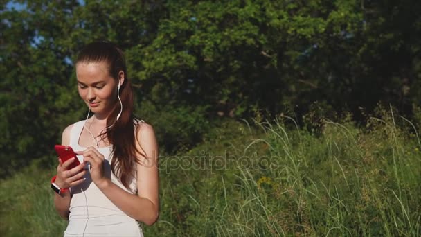 Mujer joven usando teléfono inteligente fuera en los árboles verdes fondo de la naturaleza . — Vídeos de Stock