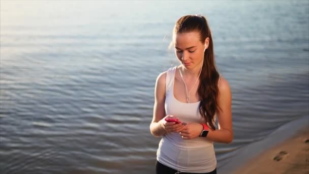 Woman walking on the sand beach chatting with her friends using her smartphone. — Stock Video